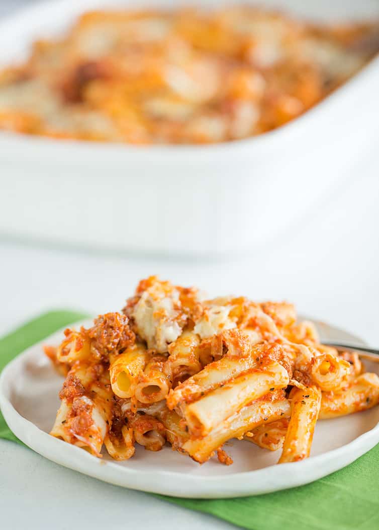 A plate of baked ziti with the casserole pan in the background.