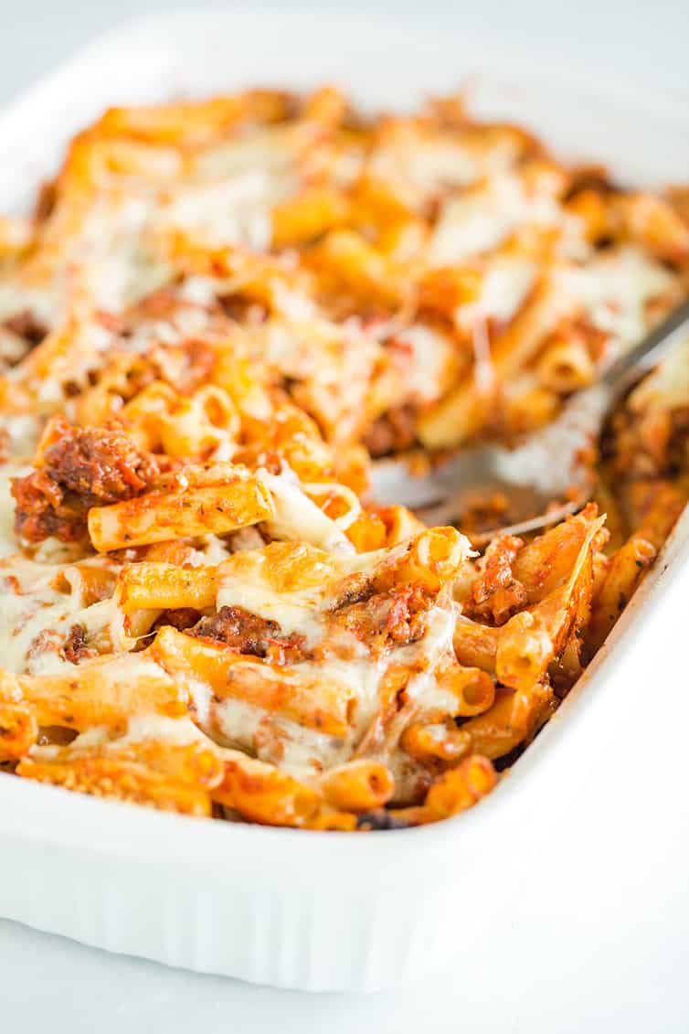 Spooning out a scoop of baked ziti from the pan.