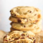 One chocolate chip cookie split in half in front of a stack of cookies.