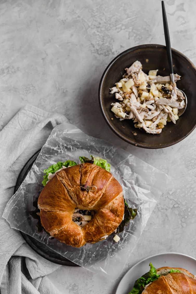 An overhead photo of a chicken salad sandwich on croissant with a bowl of chicken salad filling next to it.