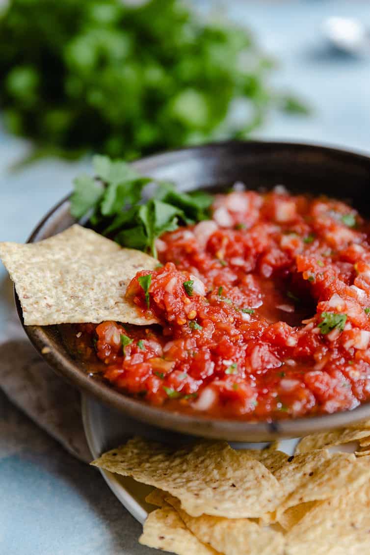 A bowl of salsa with a chip dipped into it.