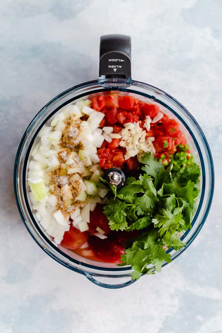 All of the salsa ingredients in the bowl of a food processor.