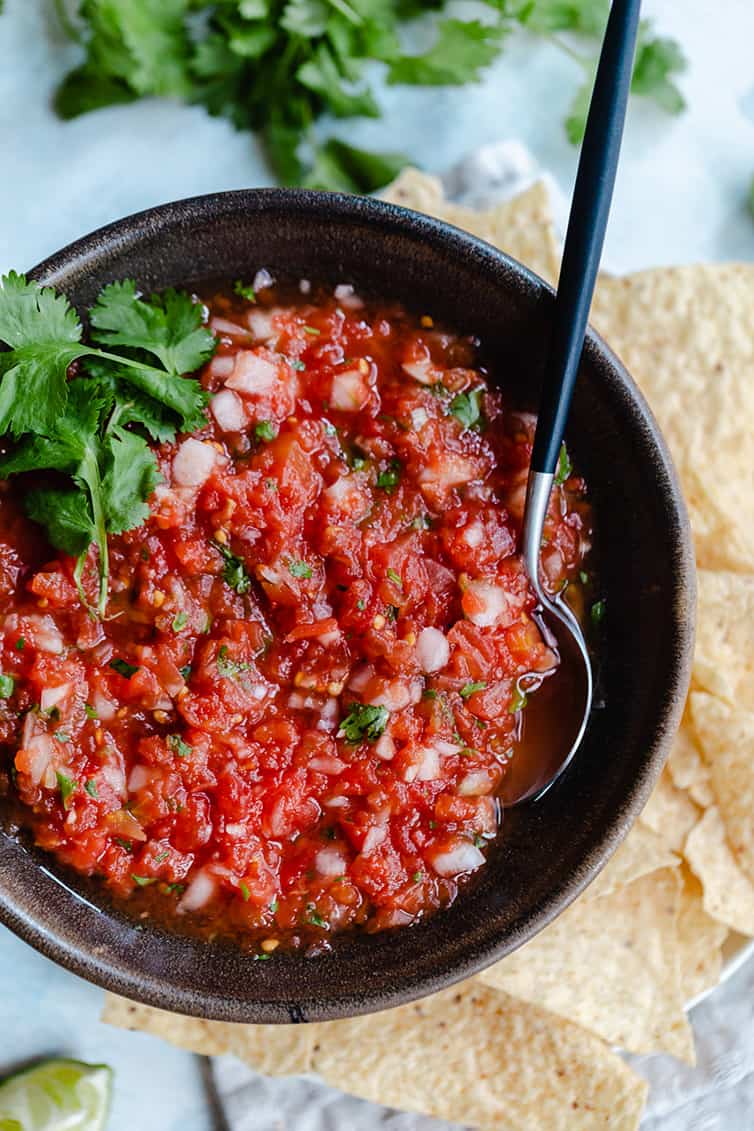 A bowl of salsa with a spoon in it and tortilla chips on the side.