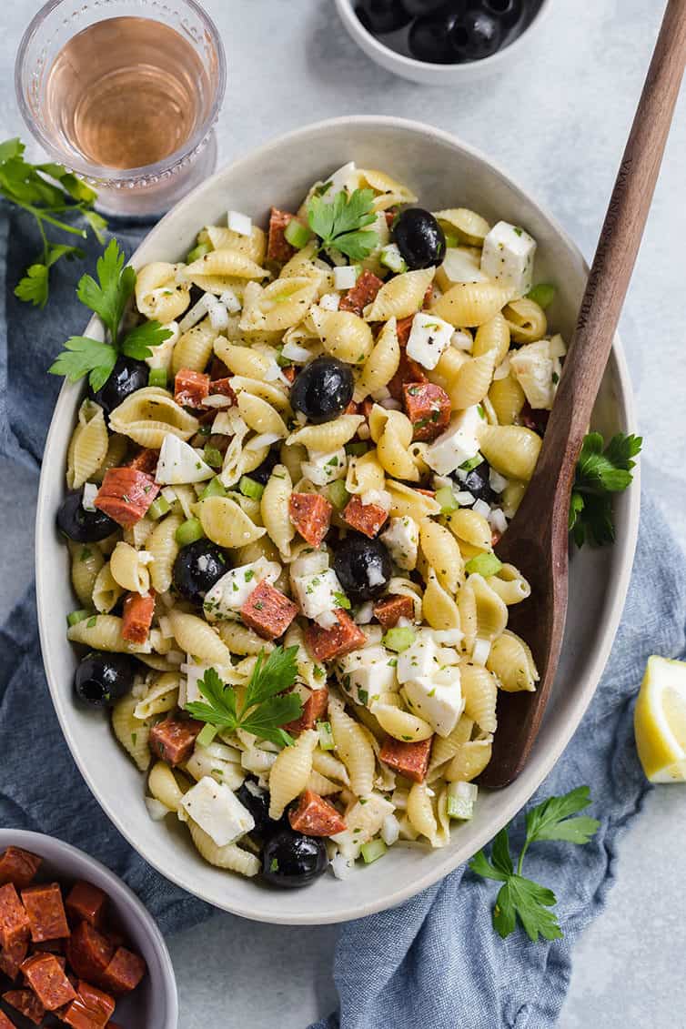 A serving bowl with pasta salad and a wooden spoon.