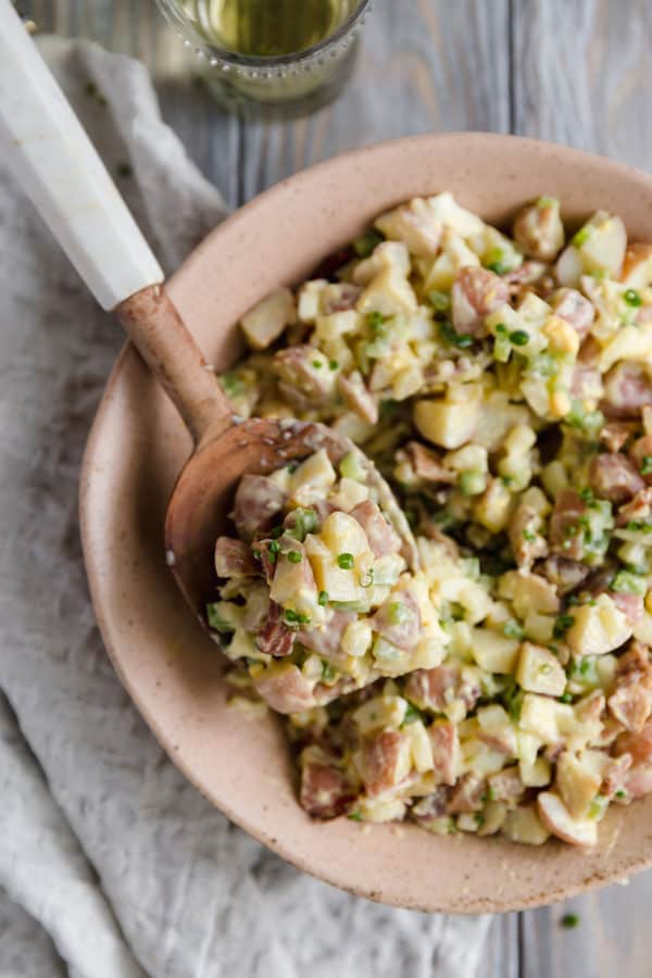A serving spoon scooping out potato salad from a bowl.