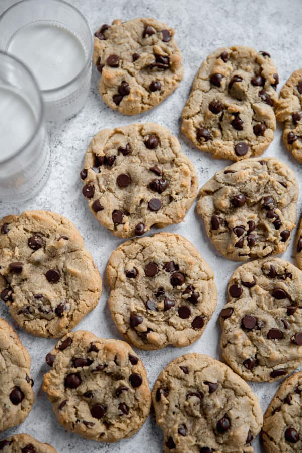 Chocolate chip cookies on wax paper with glasses of milk.