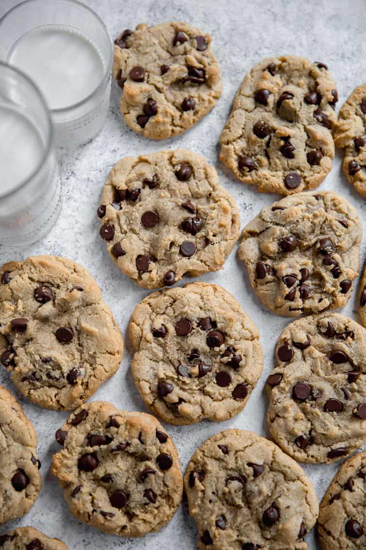 Chocolate chip cookies on wax paper with glasses of milk.