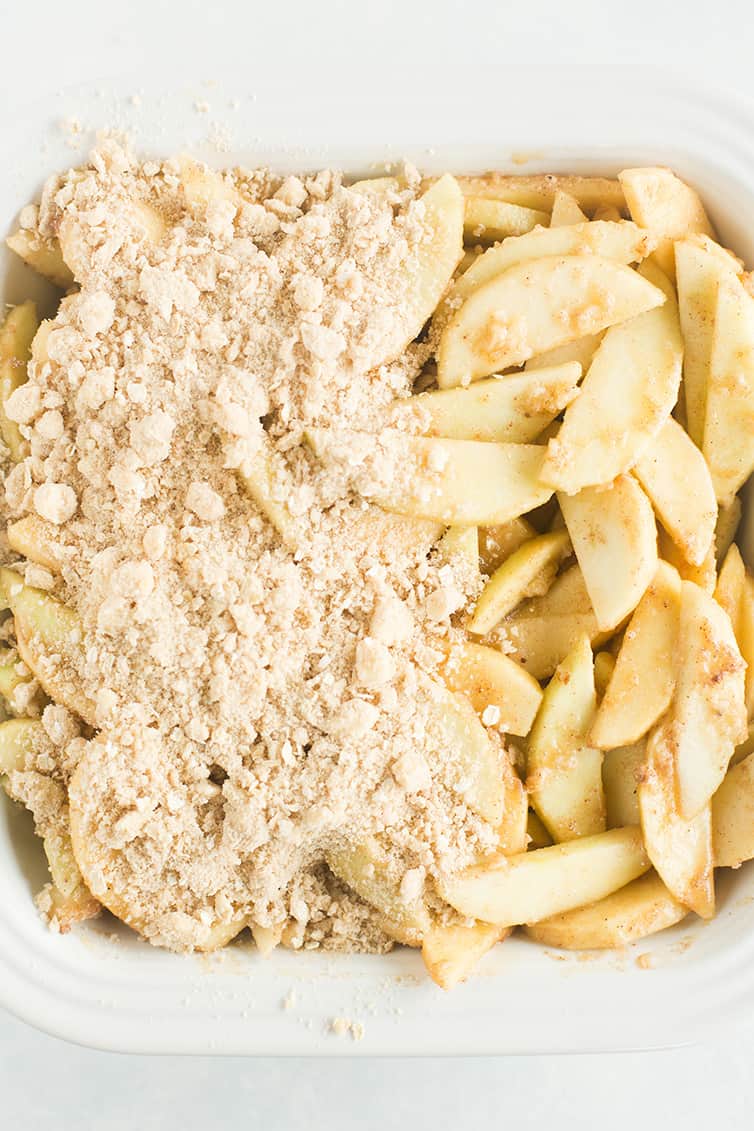 Apple crisp filling in a pan with topping over half of it.