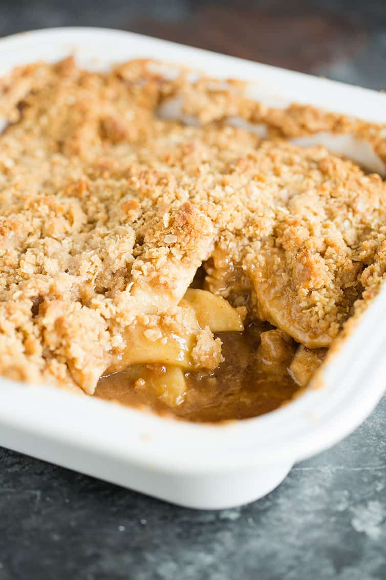 A pan of baked apple crisp with a corner scooped out.