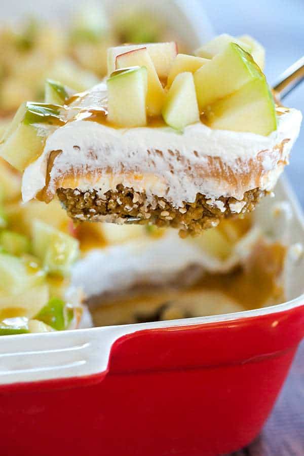 This caramel apple pudding has layers of caramel cheesecake filling, caramel pudding, a whipped cream topping, apples, and peanuts all on top of a gingersnap crust.