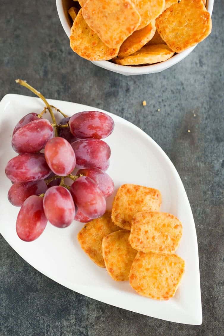 A plate of homemade cheese crackers with red grapes.