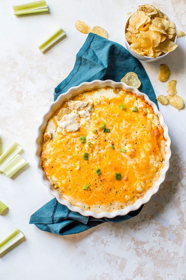 A pan of cheesy buffalo chicken dip with celery and chips for dipping.