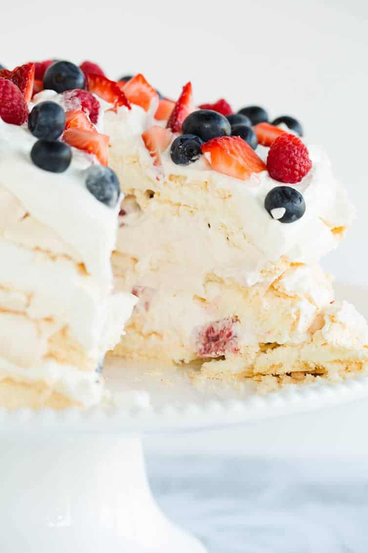 Pavlova layer cake sliced into with whipped cream and berries.