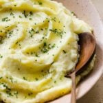 A close-up photo of mashed potatoes swirled in a bowl with a wooden spoon.