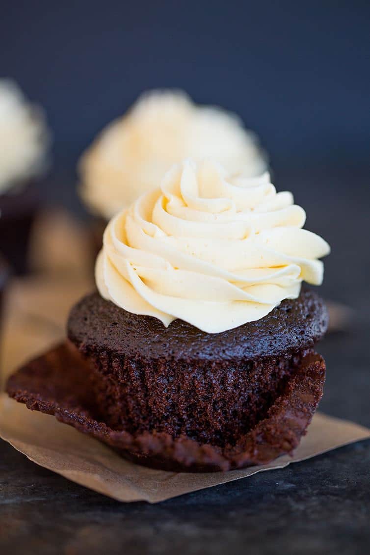 A chocolate cupcake with vanilla frosting with the paper wrapper pulled off halfway.