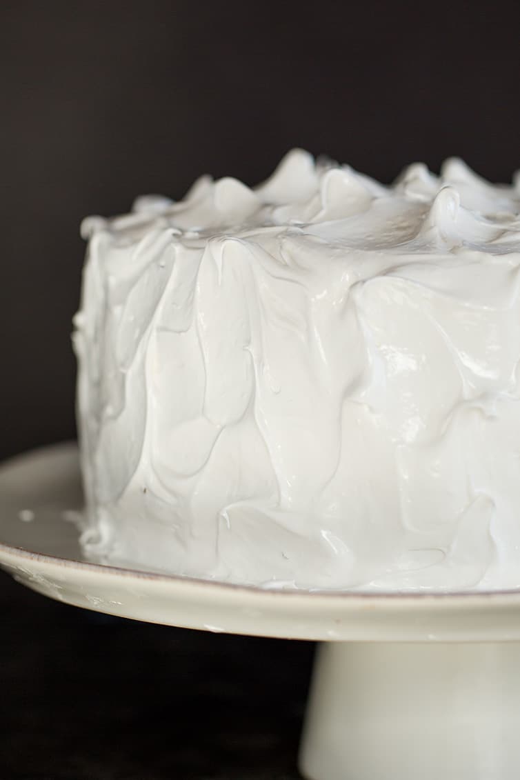A devil's food cake covered in seven minute frosting on a cake stand.