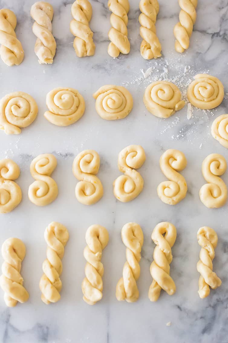 Shaped Koulourakia cookies on a marble pastry board.