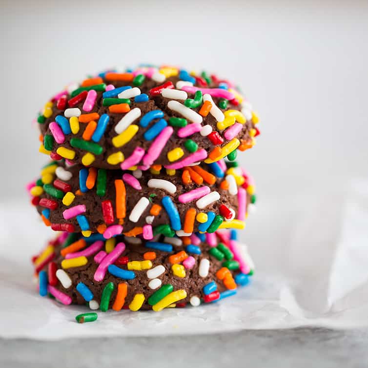 Three chocolate crinkle sprinkle cookies stacked on top of one another.