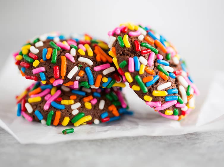 Three chocolate crinkle sprinkle cookies on parchment paper.