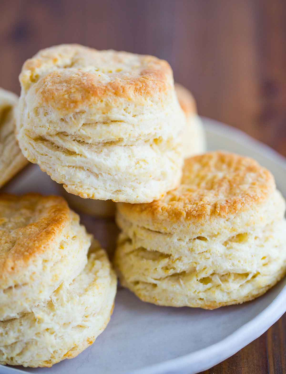 Fluffy and flaky buttermilk biscuits stacked on a white plate.