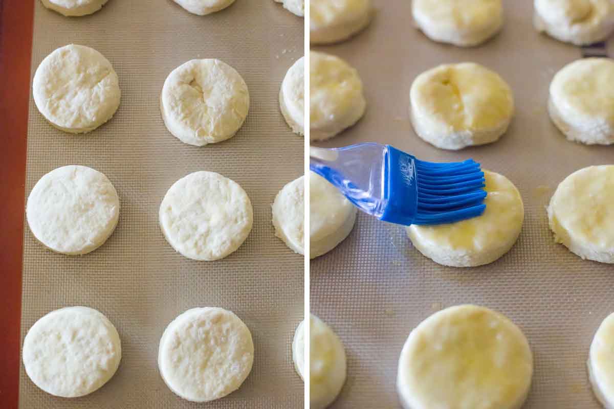 Rounds of biscuit dough on a baking sheet and being brushed with melted butter.