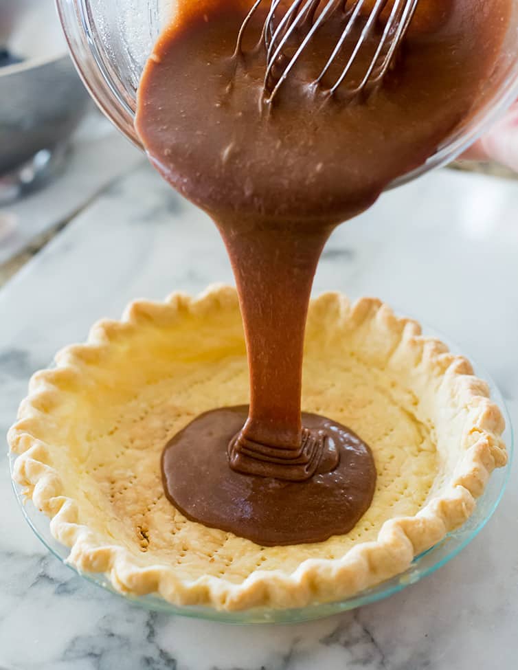 Pouring the chocolate batter for chocolate chess pie into a prepared pie shell.