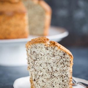 A slice of chocolate chip chiffon cake on a plate with the whole cake on a platter behind it.
