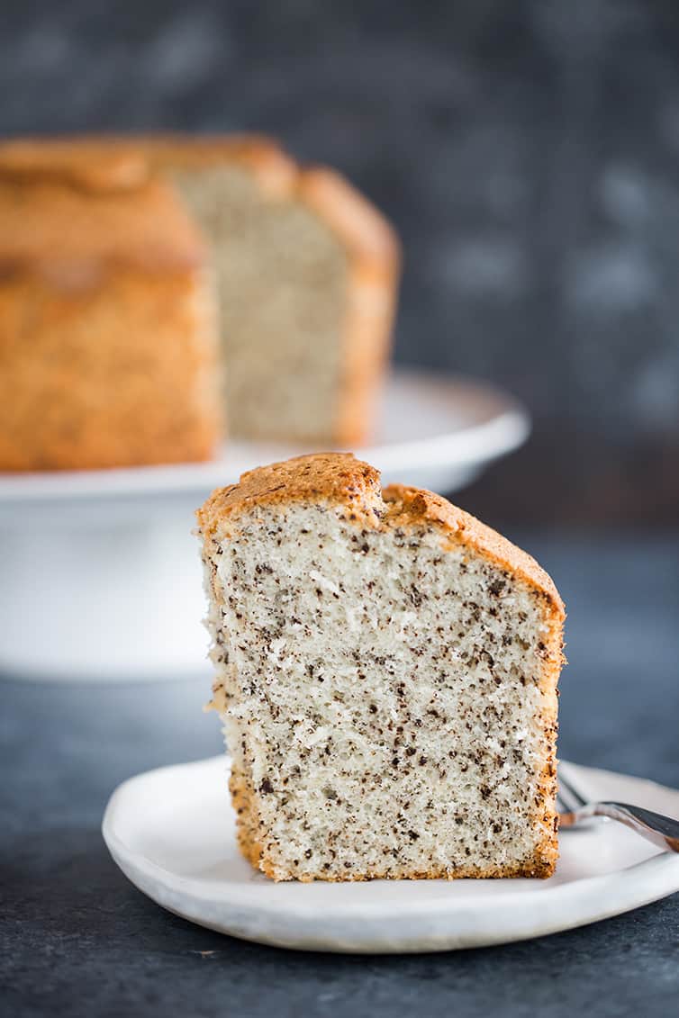 A slice of chocolate chip chiffon cake on a plate with the whole cake on a platter behind it.