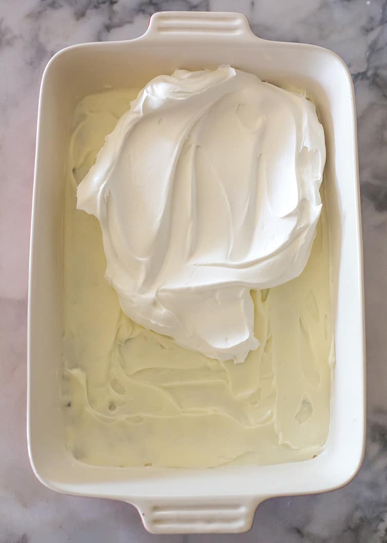 Cool Whip being spread on top of cream cheese layer of chocolate lush dessert.