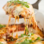 A piece of chicken parmesan being lifted out of the pan.