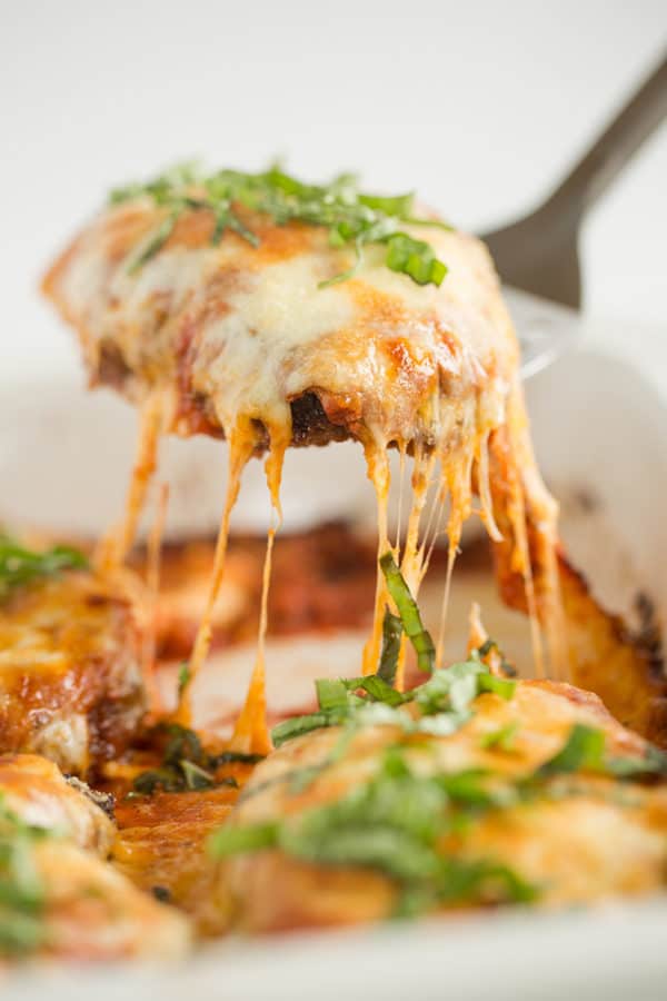 A piece of chicken parmesan being lifted out of the pan.