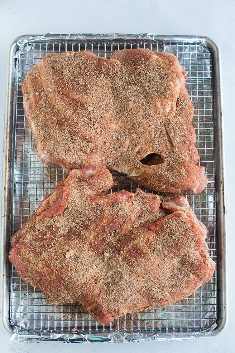 Two pieces of pork covered in rub on a wire rack.