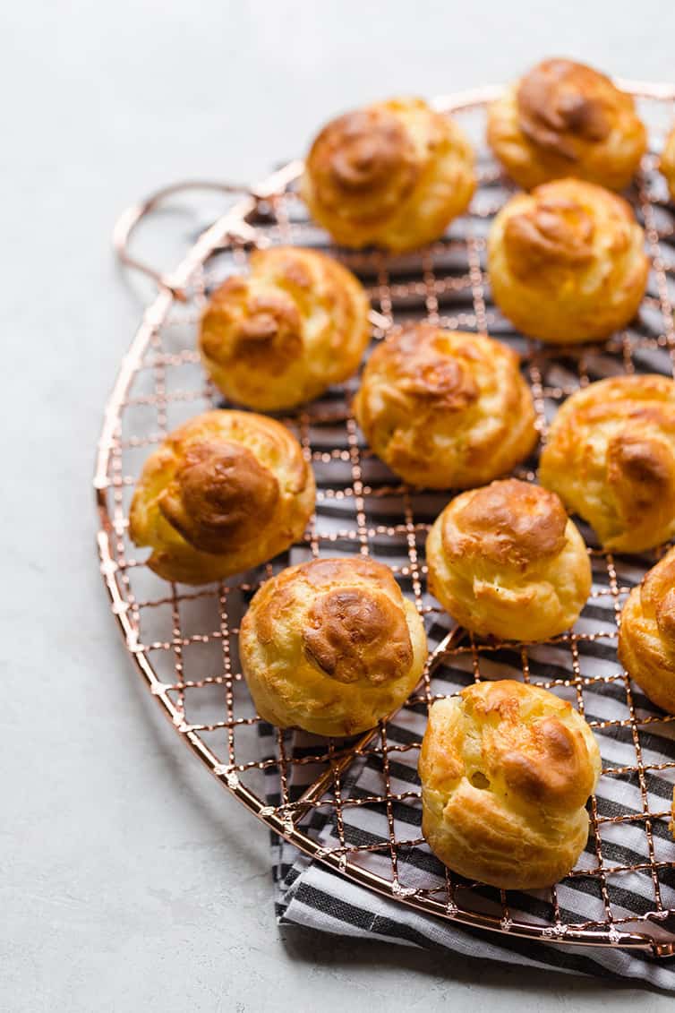 Baked gougeres on a round cooling rack.
