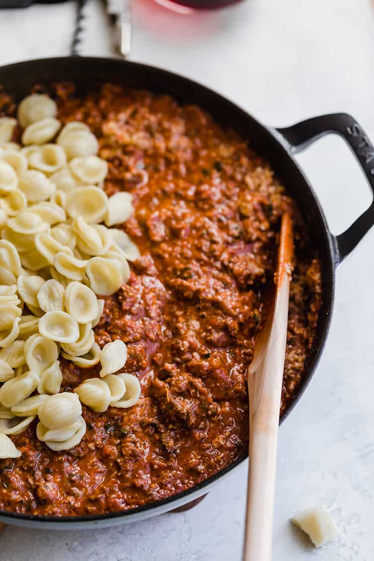 Orecchiette pasta mixed into a pan of bolognese sauce.