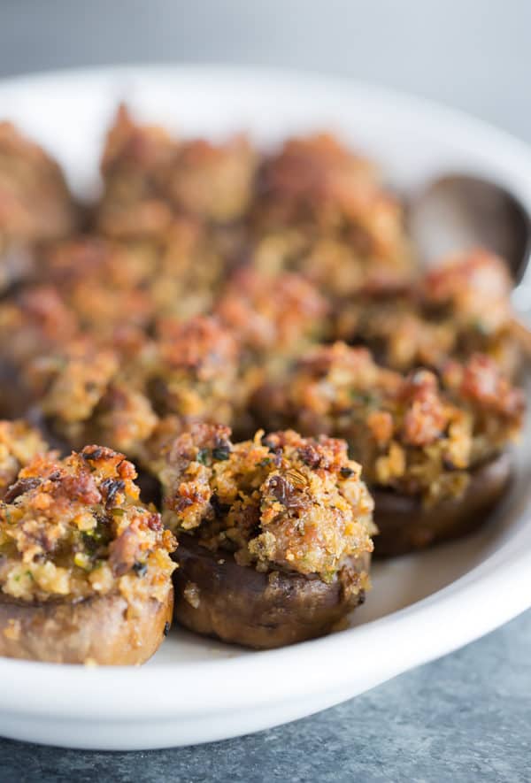 A serving platter full of sausage stuffed mushrooms.