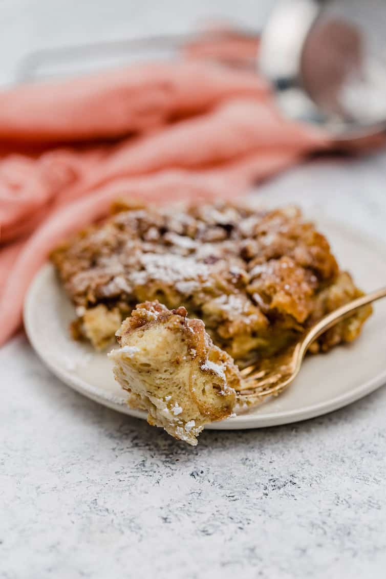 A piece of baked French toast on a fork with a piece on a plate in the background.