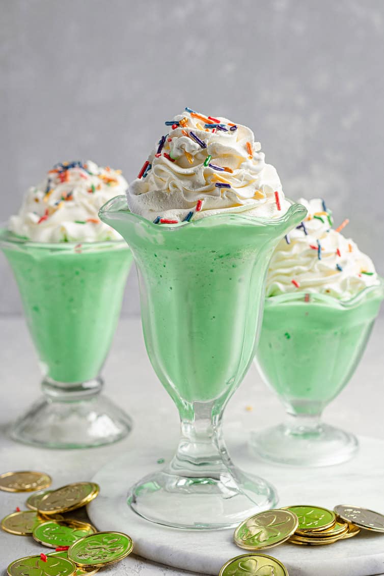 Three milkshake glasses filled with green shamrock shakes.
