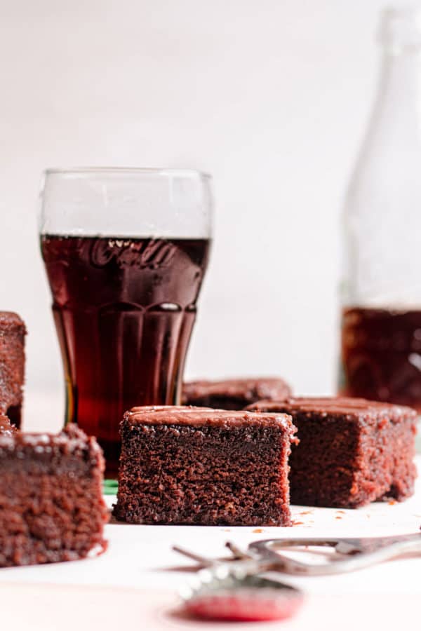 Pieces of chocolate cake in front of glasses of Coca Cola.