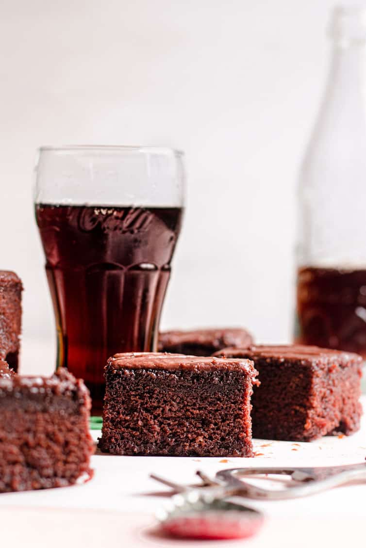 Pieces of chocolate cake in front of glasses of Coca Cola.