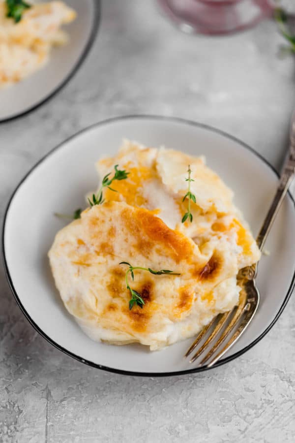 Small white bowl holding a serving of scalloped potatoes and a fork