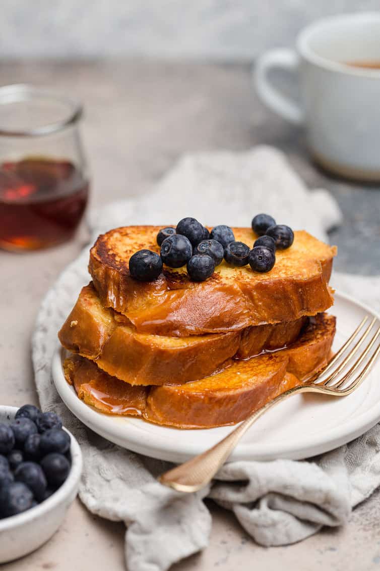 A stack of French toast on white plate with blueberries on top.