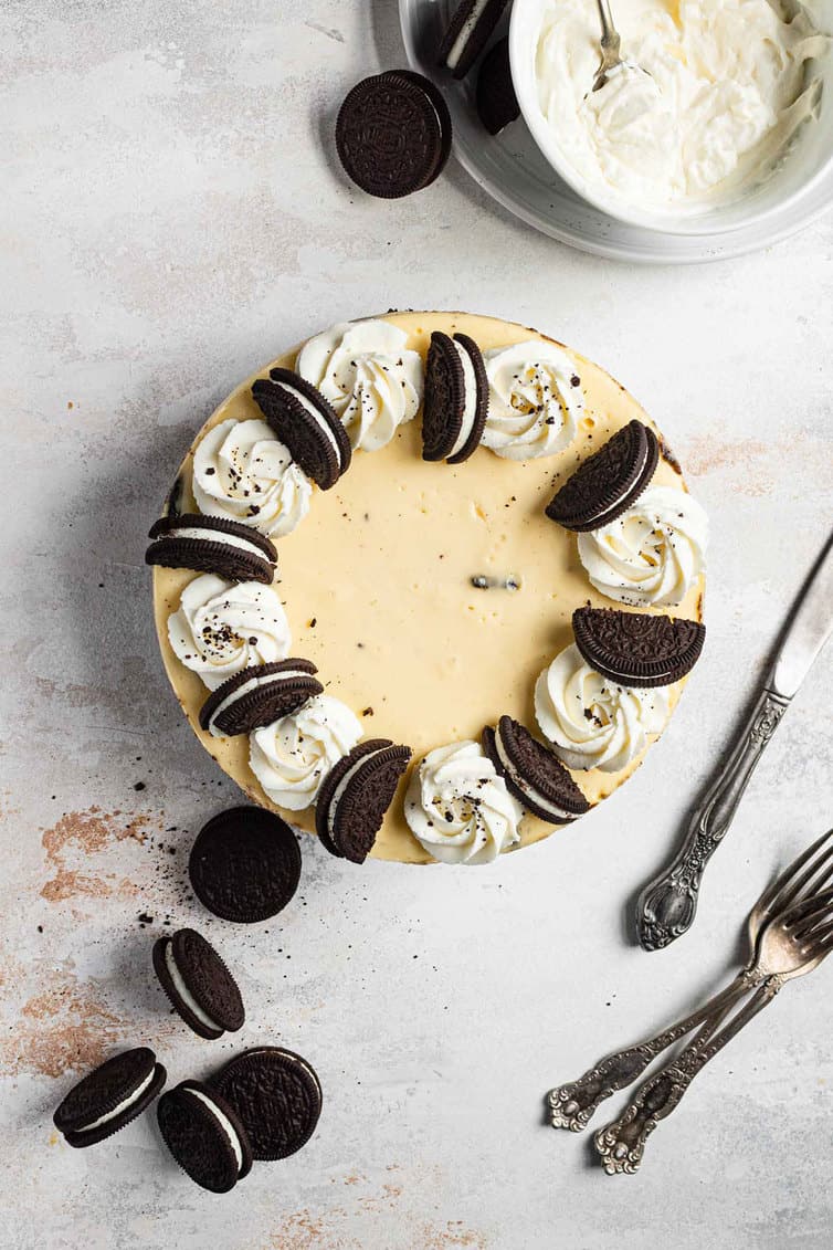 An overhead photo of Oreo cheesecake with silverware, Oreos and whipped cream around it.
