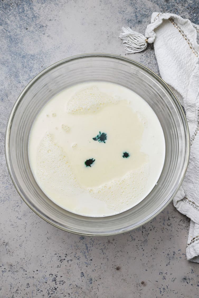 Custard ice cream base with three drops of green food coloring on surface.
