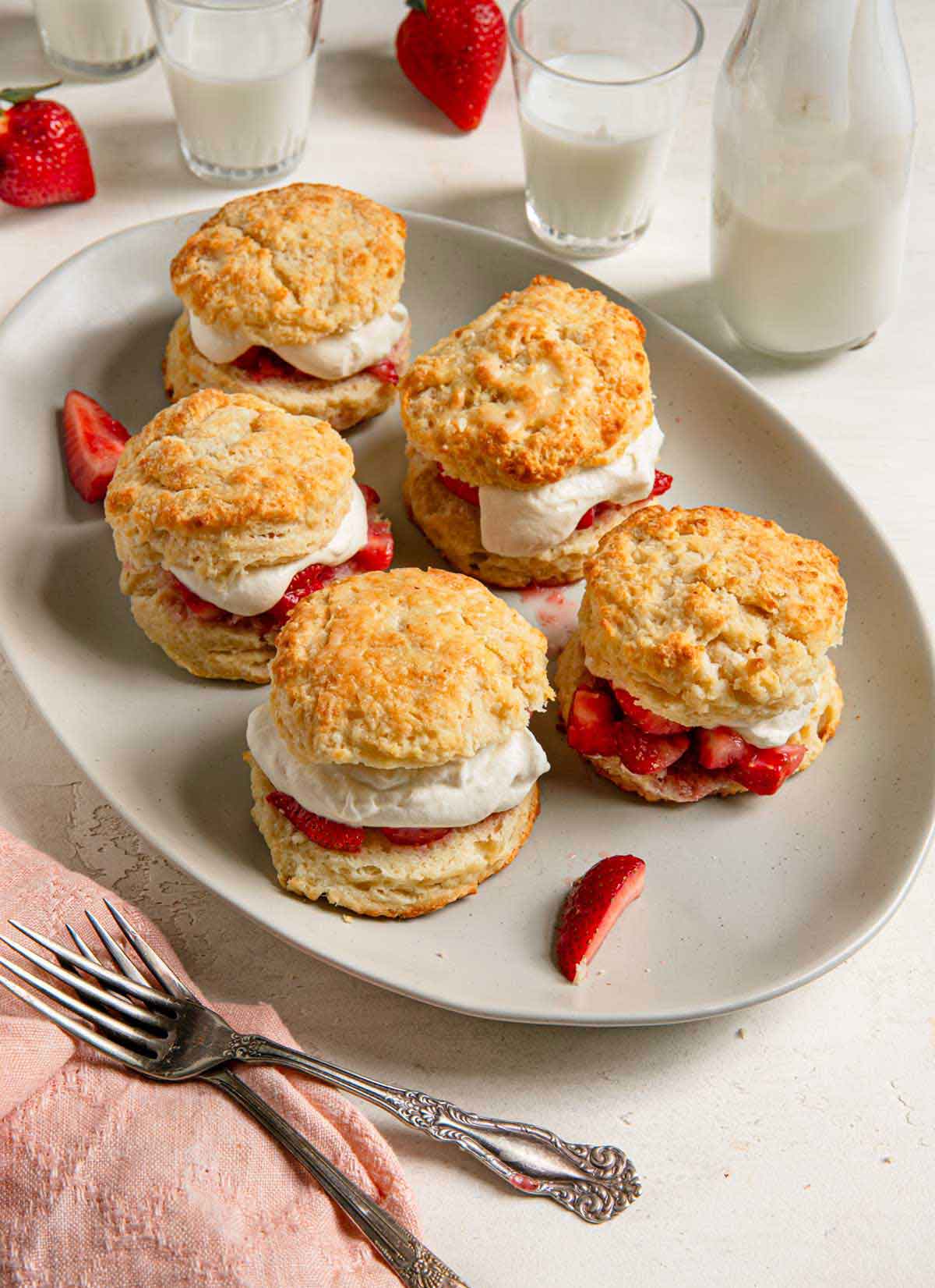 A platter of assembled strawberry shortcakes, with strawberries and glasses of milk in the background.