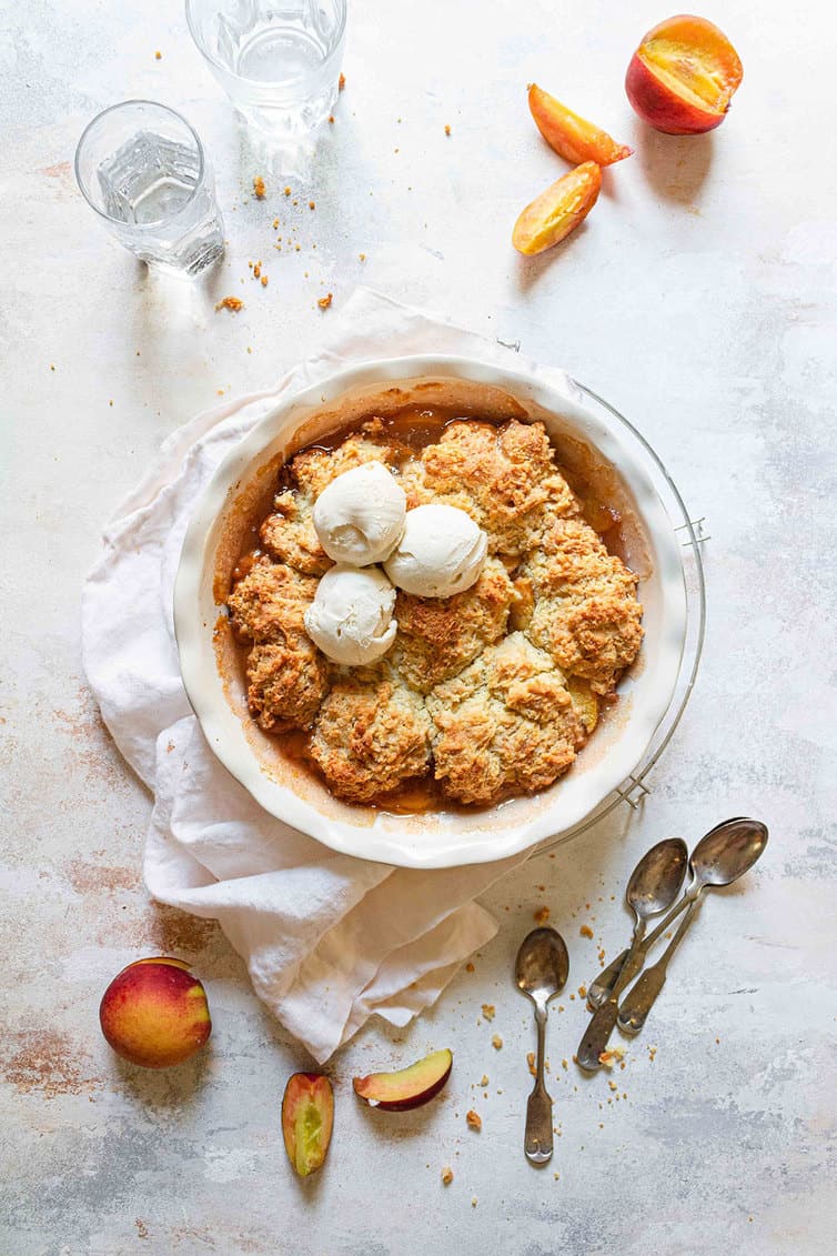 Baked peach cobbler with three scoops of ice cream on top.
