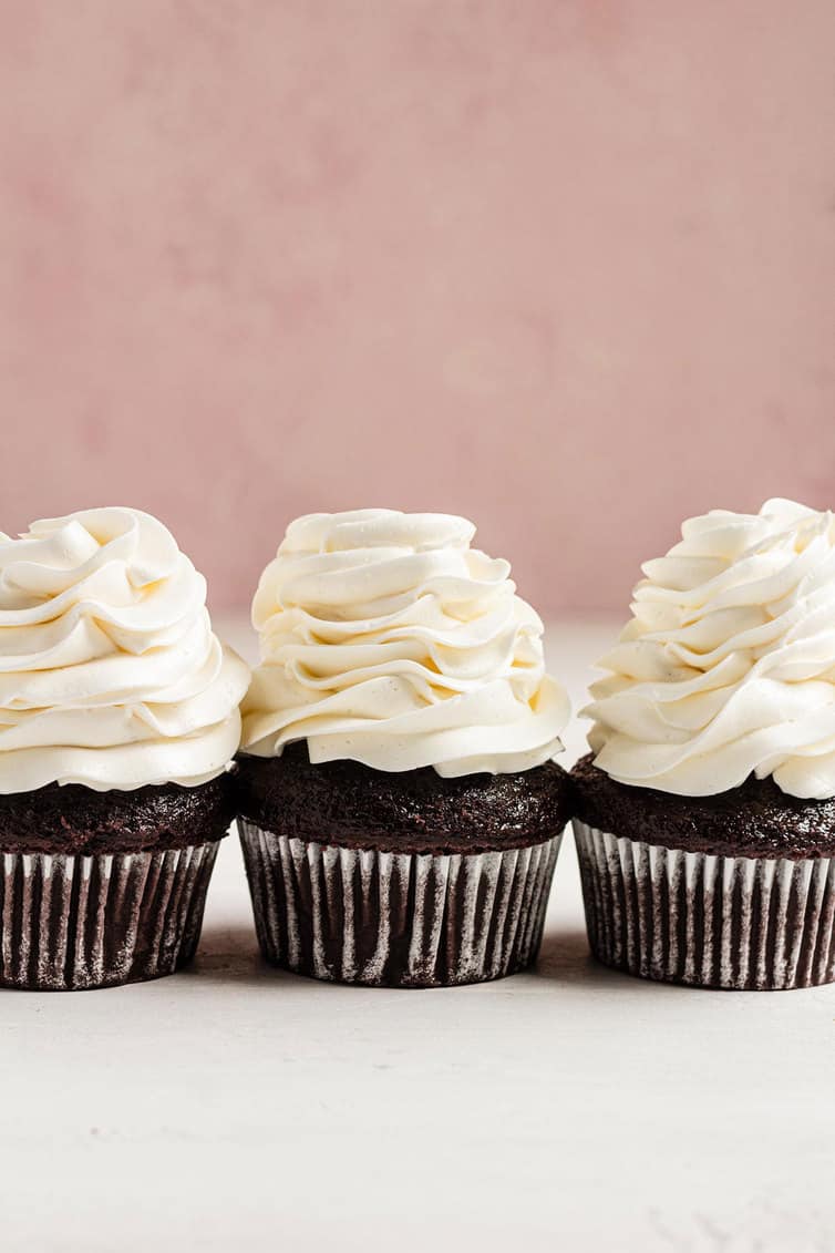Three chocolate cupcakes with Swiss meringue buttercream piped on top.