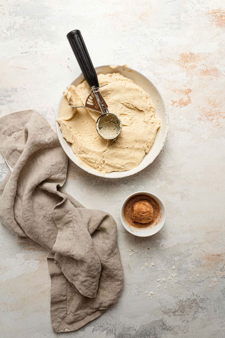 Scooping snickerdoodle cookie dough with bowl of cinnamon-sugar.