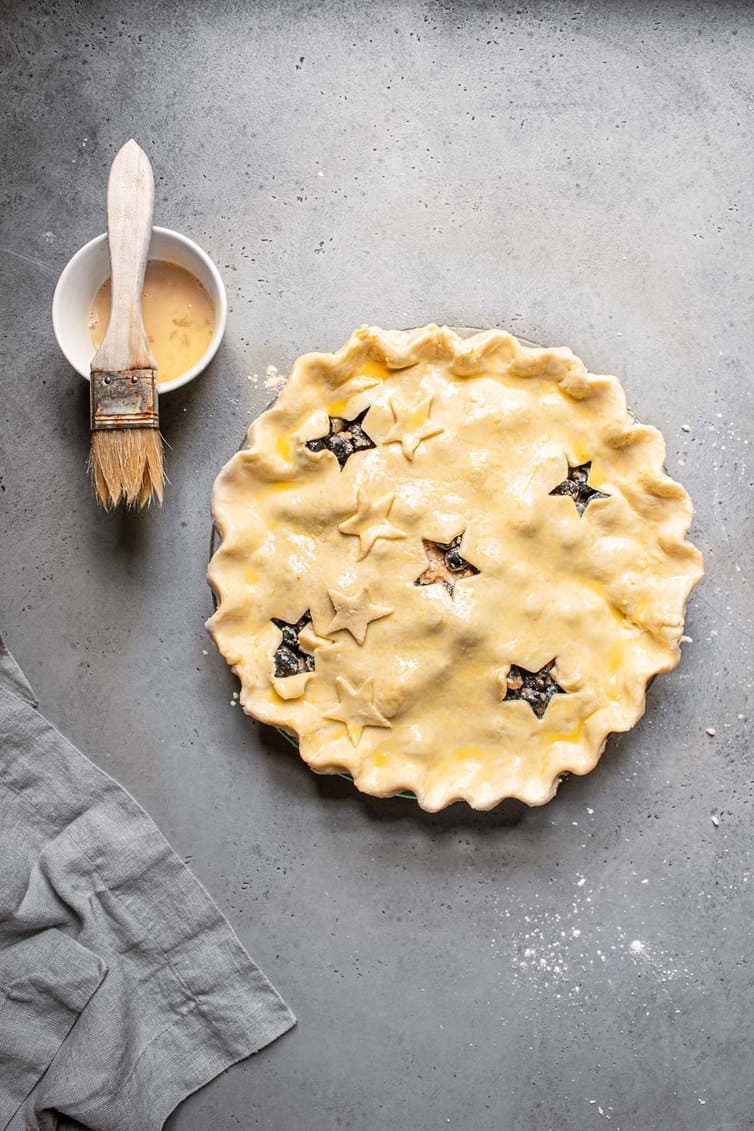 Assembled blueberry pie with egg wash before baking.