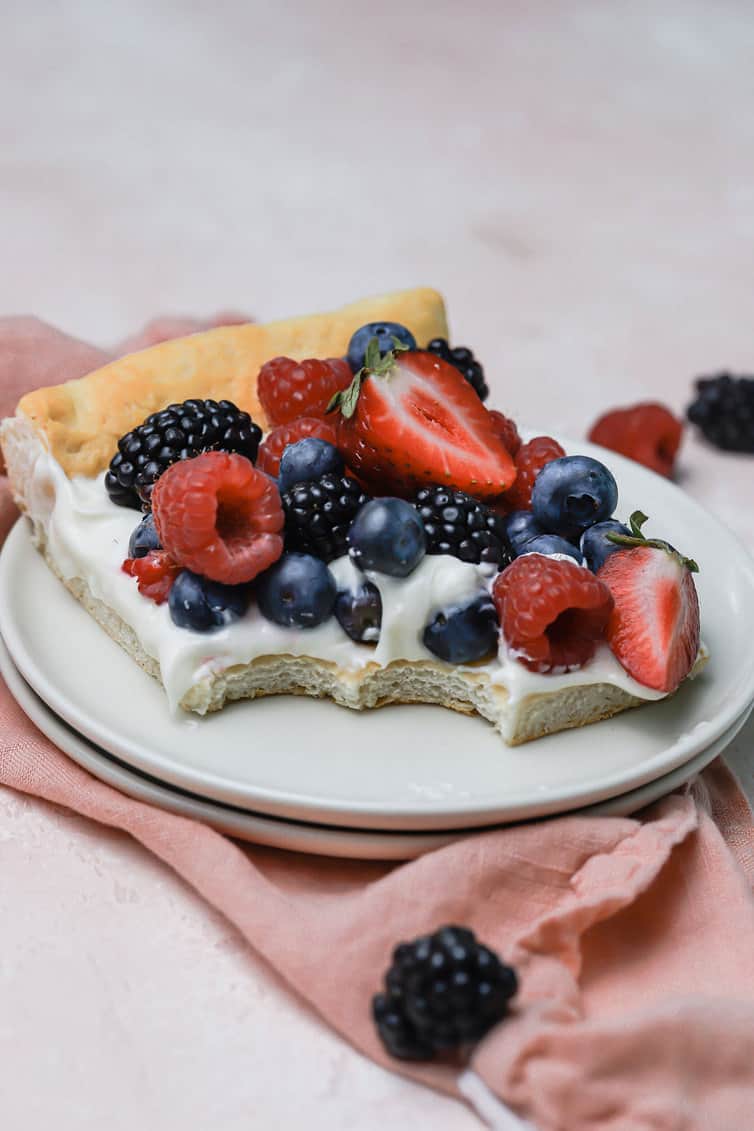 A slice of fruit pizza on a plate with two bites taken out.