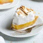 A slice of lemon meringue pie on a white plate with a fork.